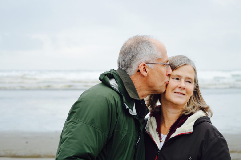 An older man kissing his wife on the cheek on a beach in Northern Ireland