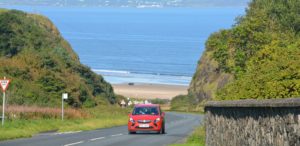 A red car driving up a coastal road on the norther coast of Northern Ireland